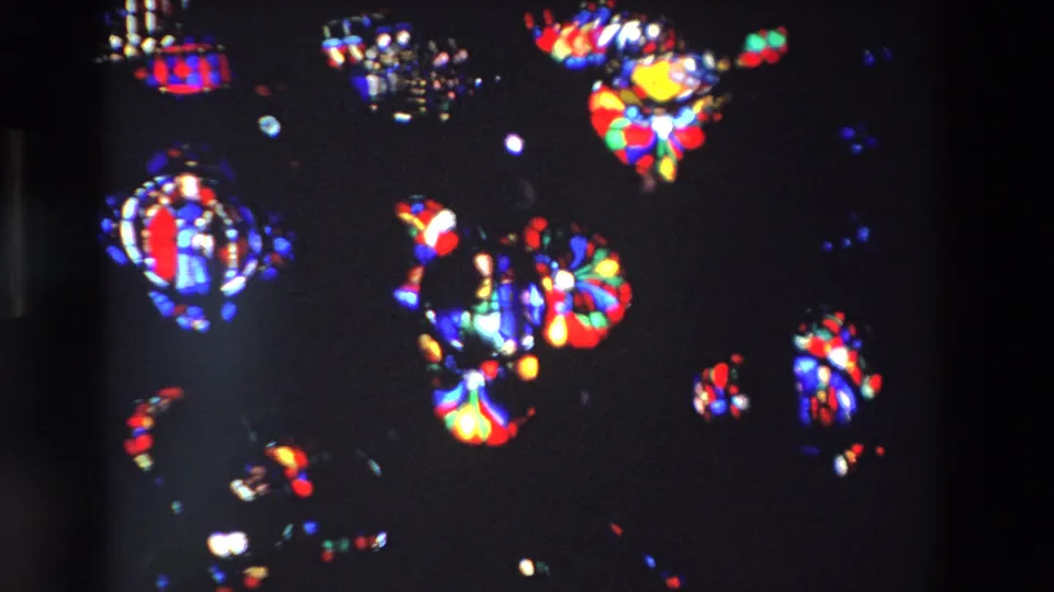 1969 Paris 8mm frame with saturated stained glass shapes, including circular forms and brighter multicolor sections on a dark ground.