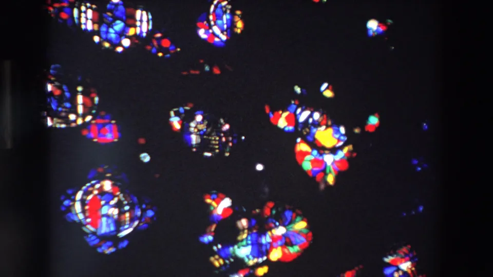 1969 Paris 8mm frame showing softly focused stained glass medallions, bright colored glass patches, and dark surrounding window space.