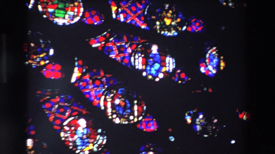 1969 Paris frame of cathedral stained glass with small robed figures and patterned red, blue, and white glass set in darkness.