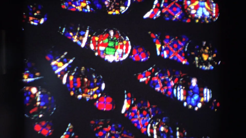 1969 Paris 8mm frame showing clustered stained glass medallions with red, blue, green, and yellow panes inside a shadowed cathedral setting.