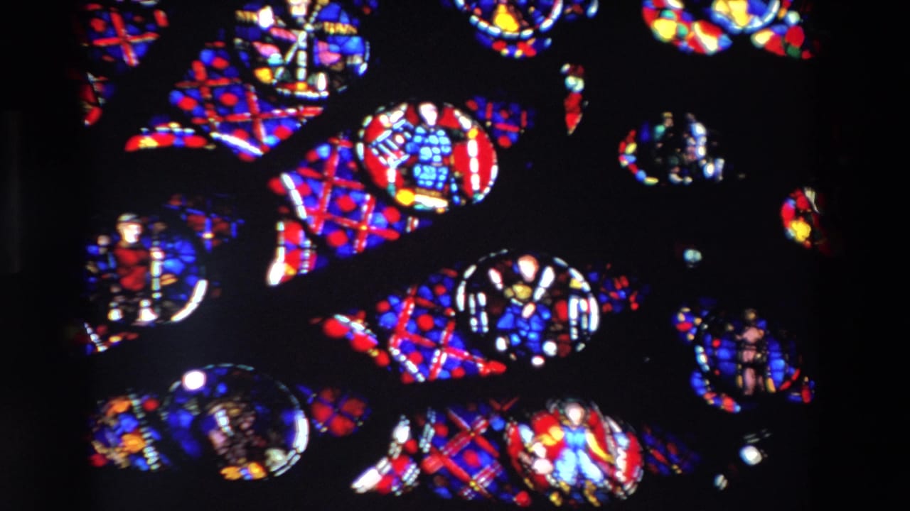 1969 Paris 8mm frame showing saturated red, blue, yellow, and white stained-glass patterns with small religious figures set in dark leadwork.
