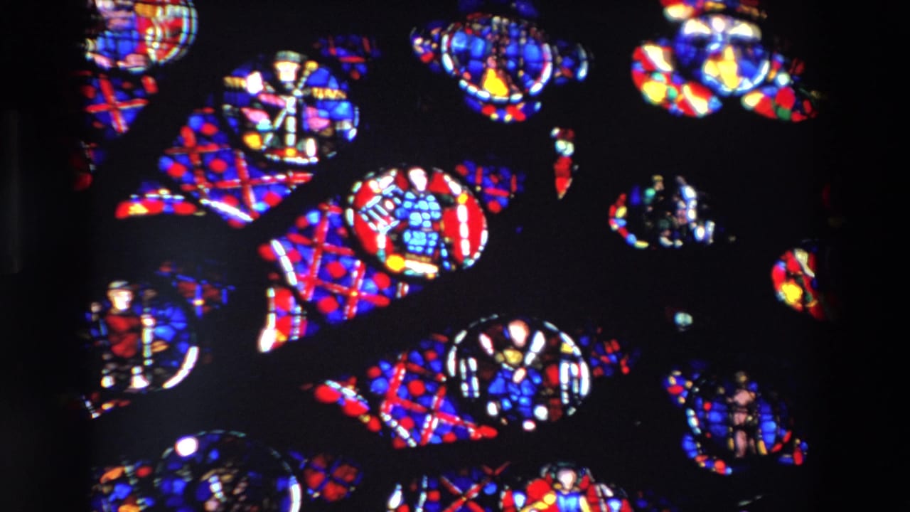 Stained glass panels with repeated colorful religious motifs in a dark window.