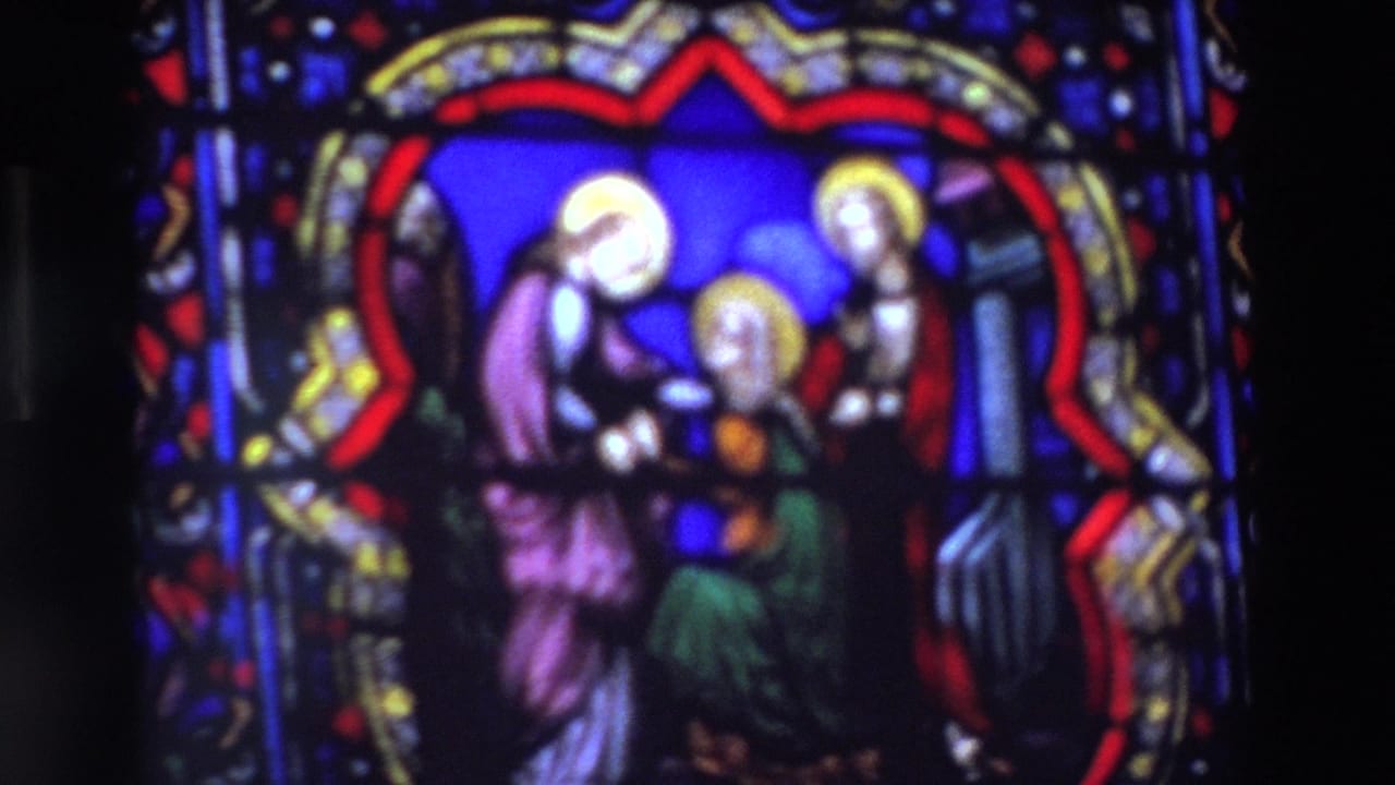 1969 Paris home-movie frame showing a soft close-up of a stained glass religious scene with haloed figures in blue, red, purple, and green glass.