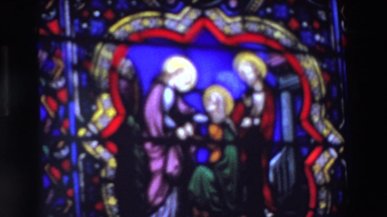 Stained glass panel with three haloed religious figures in soft focus.