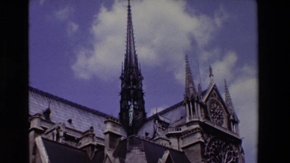1969 Paris frame showing Notre Dame Cathedral's spire rising above the roofline, with the rose window and Gothic stone ornament visible at right.