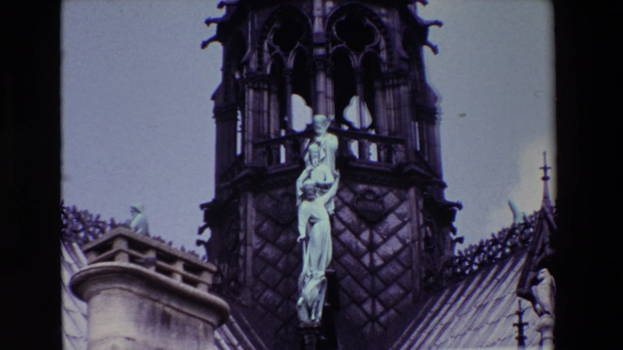 1969 Paris 8mm frame showing a Gothic cathedral spire with tracery, roof ornament, and a pale religious statue group viewed from below.