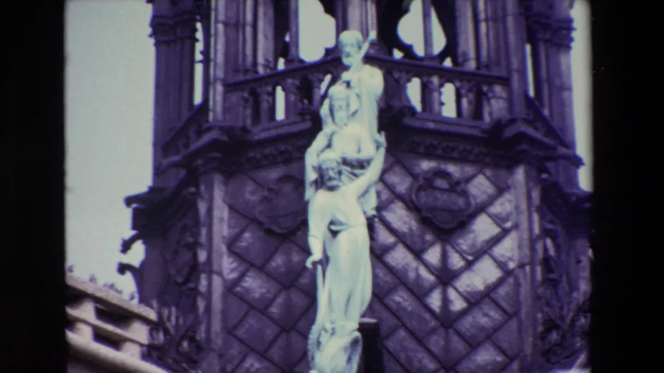 1969 Paris 8mm frame holding on a pale religious sculpture against dark Gothic stone, with tracery and carved architectural forms filling the background.