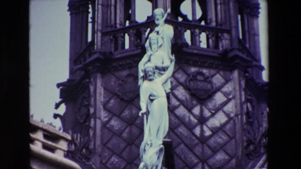 1969 Paris 8mm frame showing a pale stone statue set against carved Gothic cathedral architecture with dark scan edges and cool color shift.