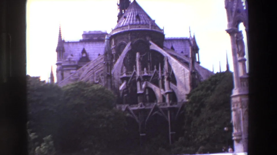 1969 Paris 8mm view of a Gothic cathedral exterior with flying buttresses, spires, roofline, trees, and a dark foreground strip from the film or camera framing.