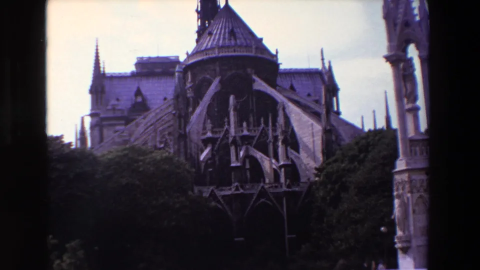1969 Paris 8mm frame holding on the cathedral exterior, with flying buttresses and spires partly obscured by trees and bordered by dark film edges.