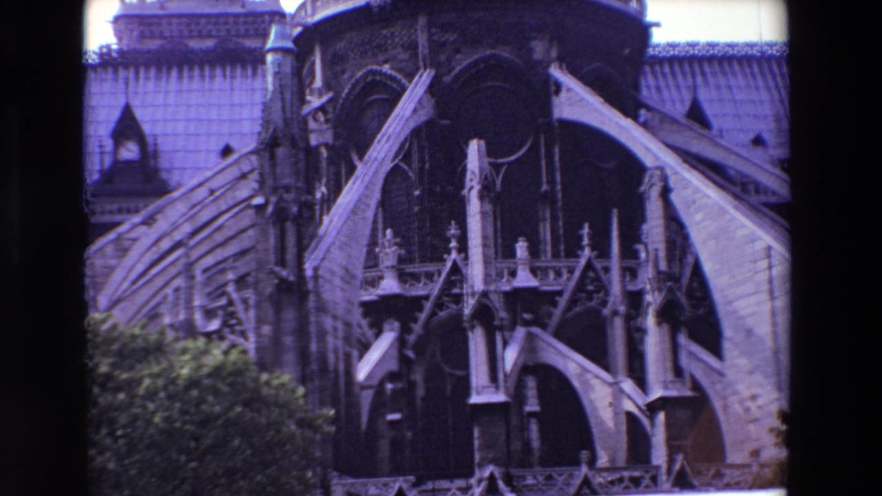 1969 Paris 8mm frame showing Notre-Dame Cathedral's exterior flying buttresses, ornate stone supports, roofline, and trees along the lower edge.