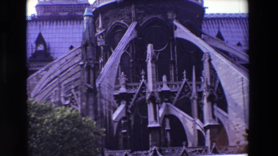 1969 Paris 8mm frame showing Notre-Dame Cathedral's exterior flying buttresses, ornate stone supports, roofline, and trees along the lower edge.