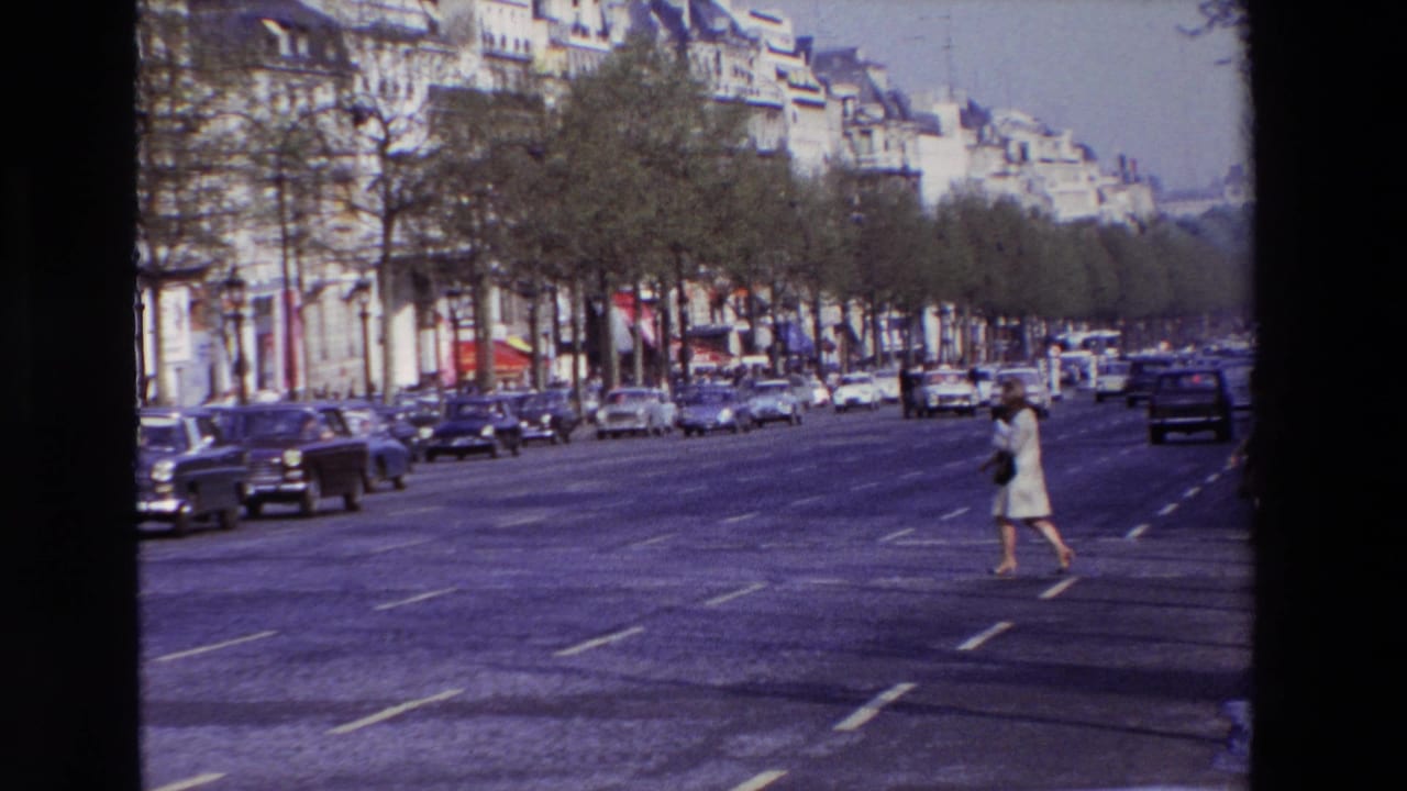 1969 Paris boulevard view with a woman in light clothing crossing multiple lanes while mid-century cars travel along a tree-lined street.