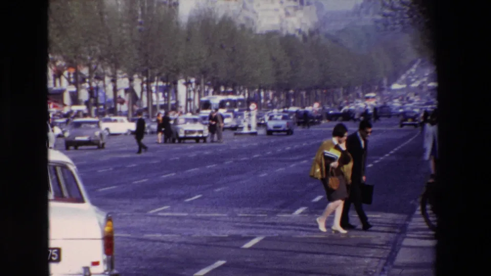 Wide Paris boulevard view from 1969 with pedestrians at the curb, moving cars, tree-lined lanes, and sidewalk activity.