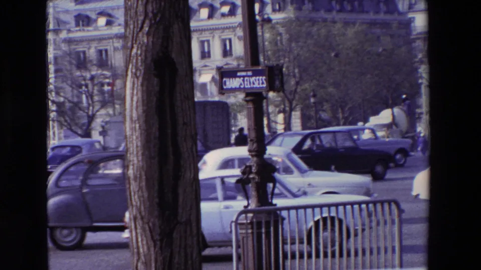 Paris street footage from the supplied 1969 metadata, with a tree trunk in the foreground, a Champs-Elysees sign, metal barriers, and older cars moving through traffic.
