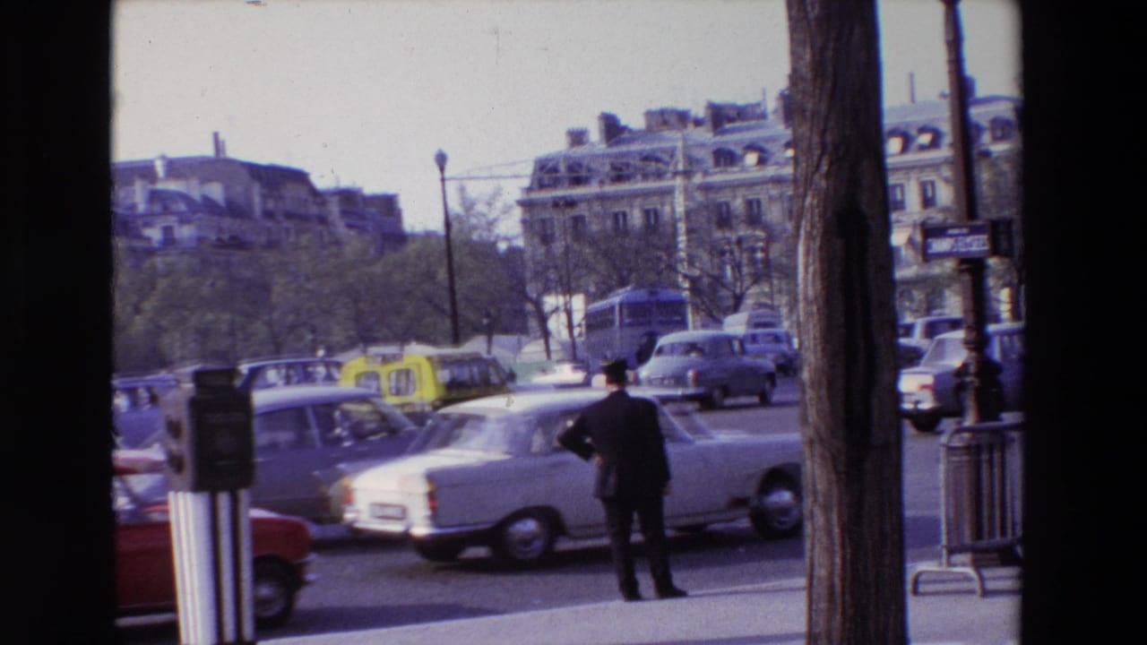 1969 Paris street traffic with classic cars, yellow taxis, sidewalk posts, trees, and a man standing near the curb.