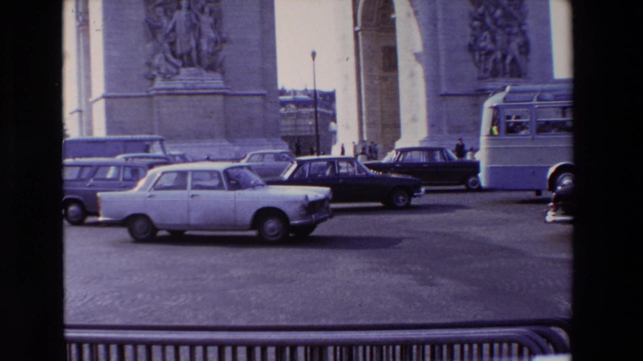 Several sedans pass in front of the Arc de Triomphe in a traffic circle.