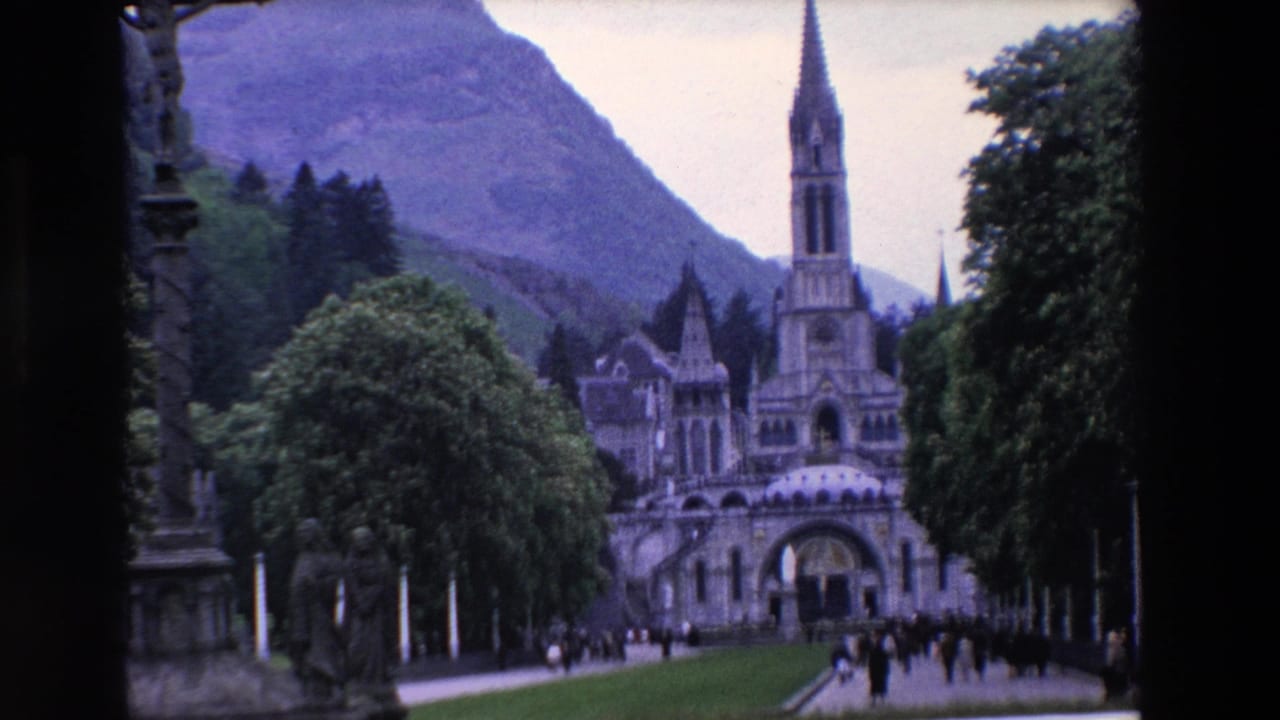 A spired church complex stands beyond lawns and trees as visitors move along the front approach.
