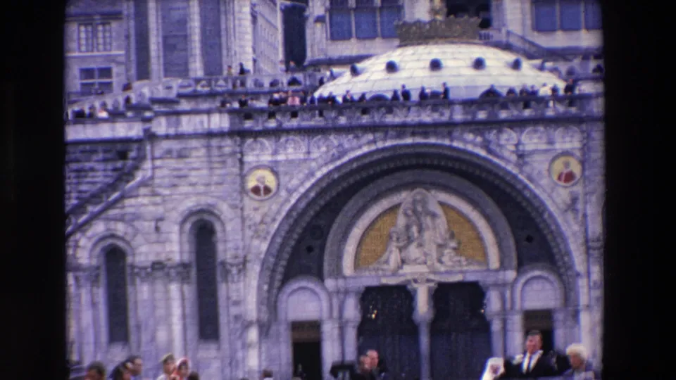 Closer 1969 8mm view of the ornate arched entrance and rounded dome of a large religious building, with adults visible on the terrace and at the lower edge of the frame.