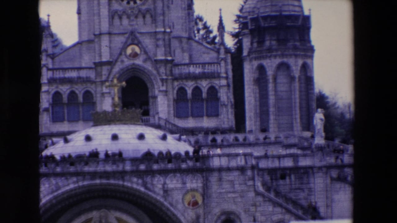 Closer view of basilica towers, arched entrance, domed roof, terrace railing, and visitors.