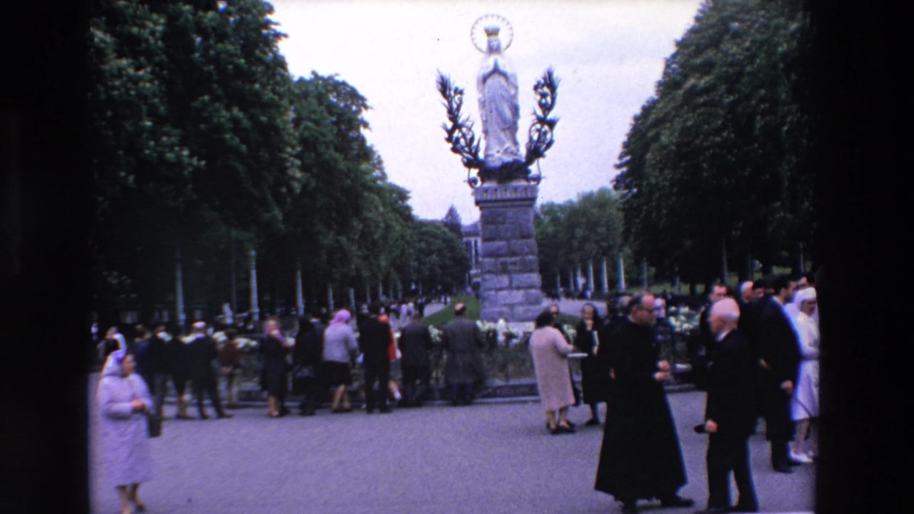 People gather around a statue on a pedestal in a tree-lined plaza.