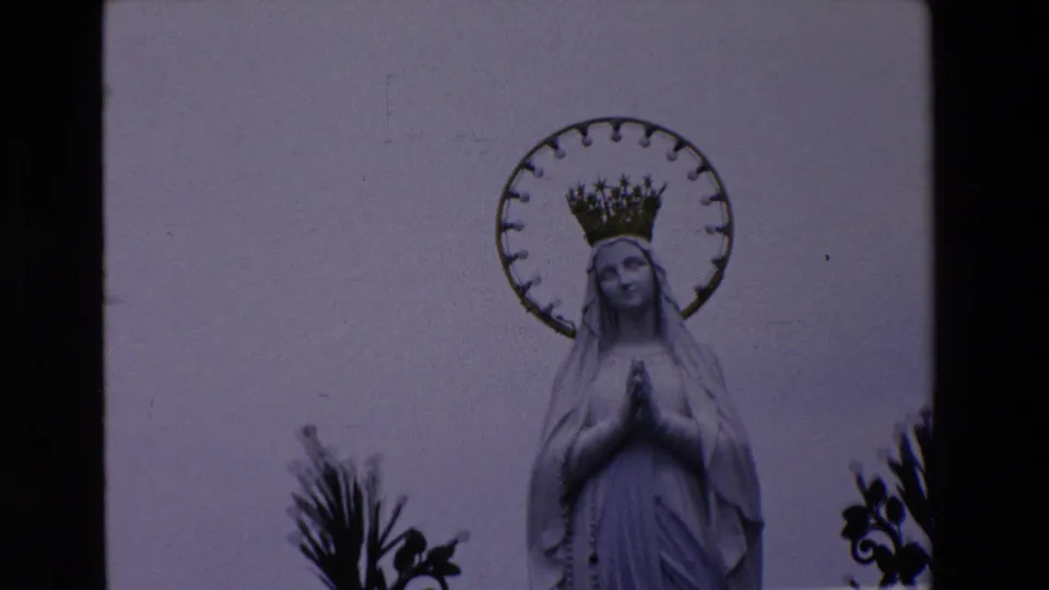 Closer 1969 Paris 8mm view of the Virgin Mary statue, emphasizing the halo, crown, veiled head, and hands held in prayer beside dark decorative metalwork.