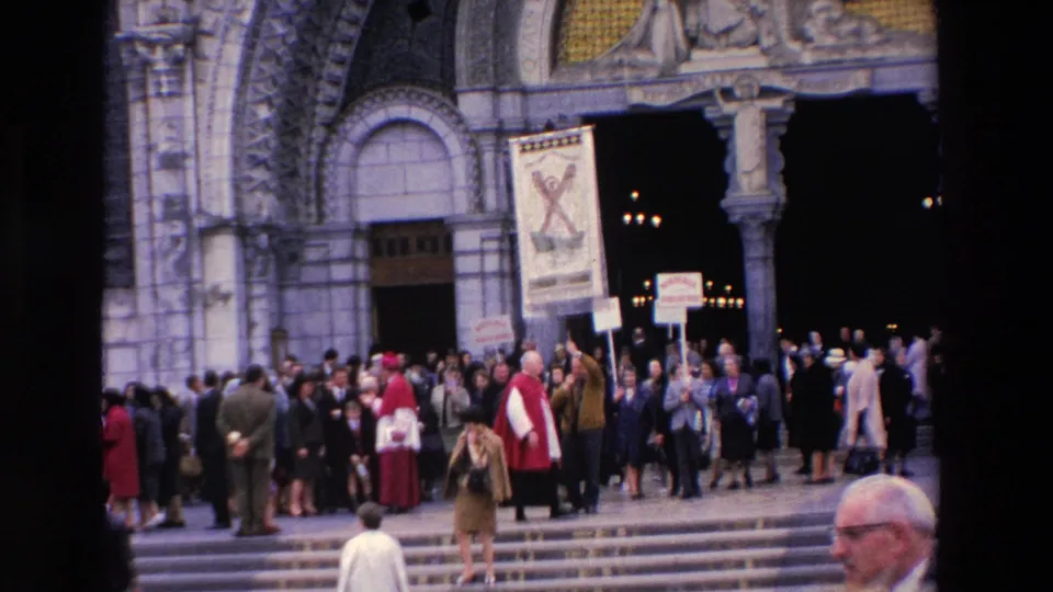 1969 Paris 8mm frame showing a crowd outside an ornate Catholic church entrance, with clergy in red vestments and French signs raised among people on the steps.