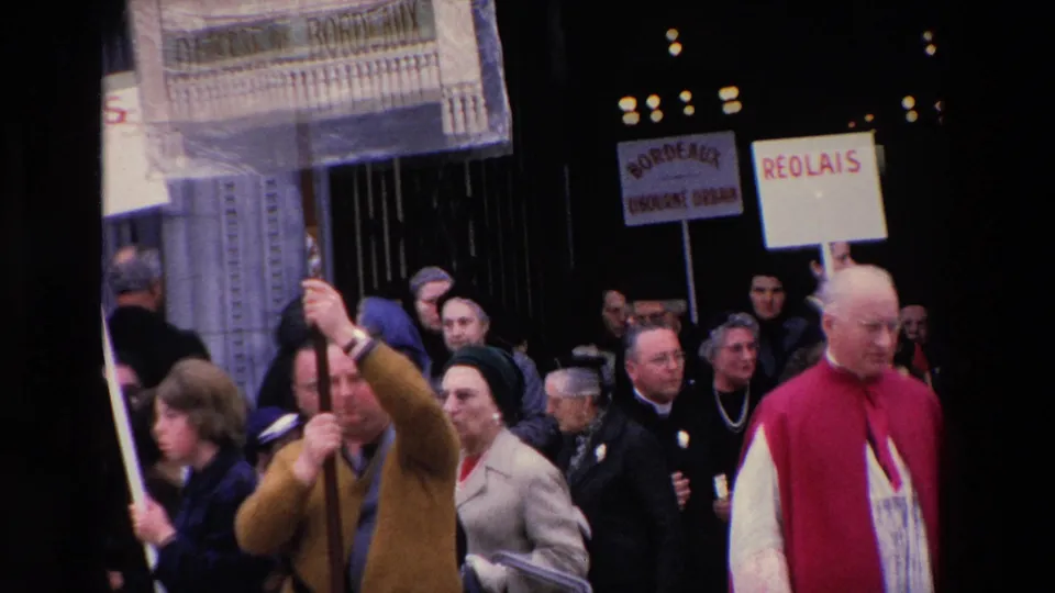 1969 Paris frame showing demonstrators and clergy near a church entrance, with placards including Bordeaux and Réolais visible above the crowd.