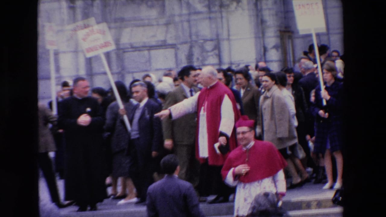 In Paris, France, supported by clip metadata, Catholic clergy in red and white vestments move among a dense crowd on stone church steps as placards are held overhead.