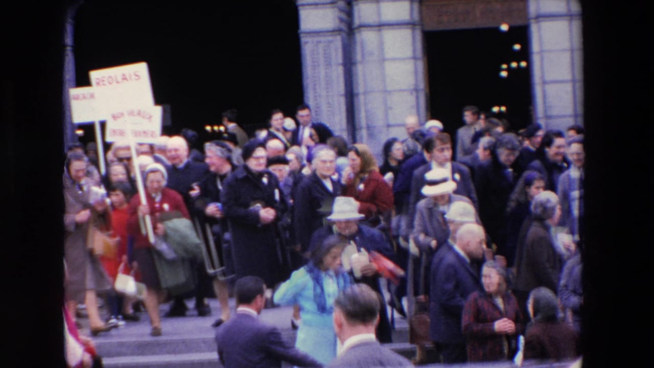 Large crowd clustered at a stone entrance with placards and clergy visible.