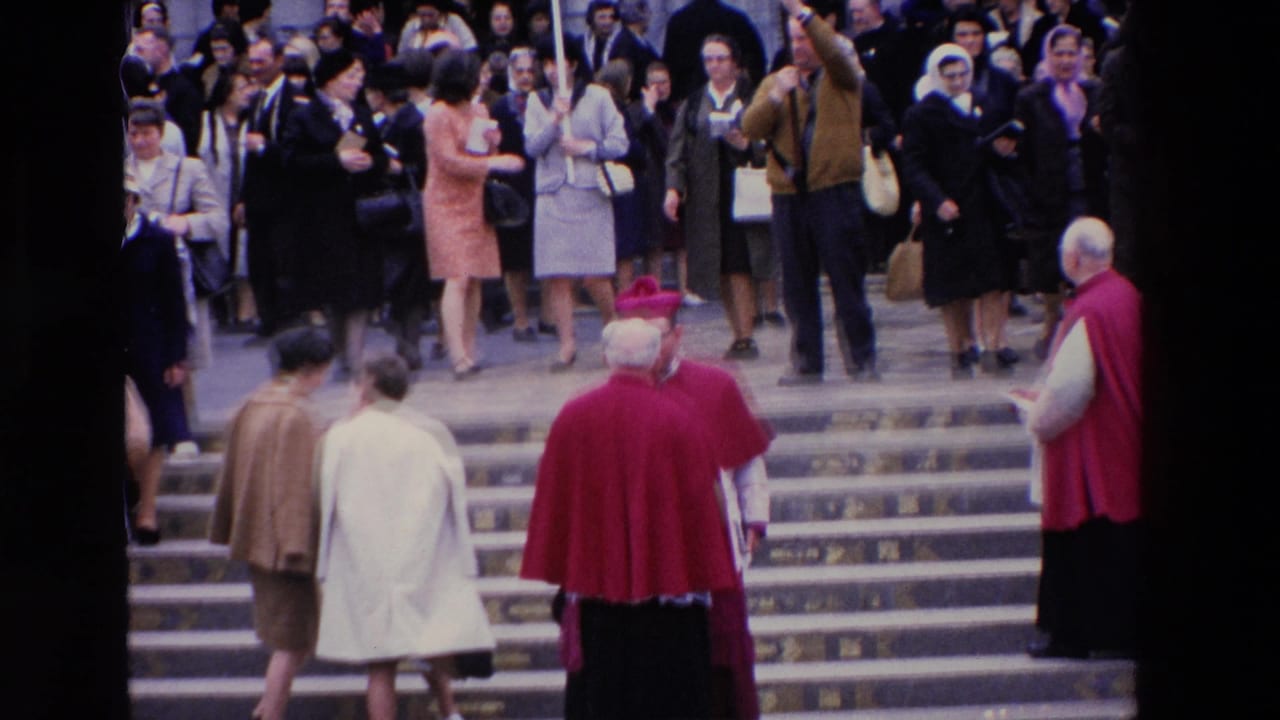1969 Paris home-movie frame showing clergy in red vestments moving down stone steps while spectators watch from the entrance area.