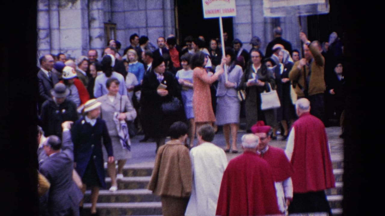 1969 Paris frame with onlookers clustered around stone steps, clergy in red vestments, uniformed personnel, and placards above the crowd.