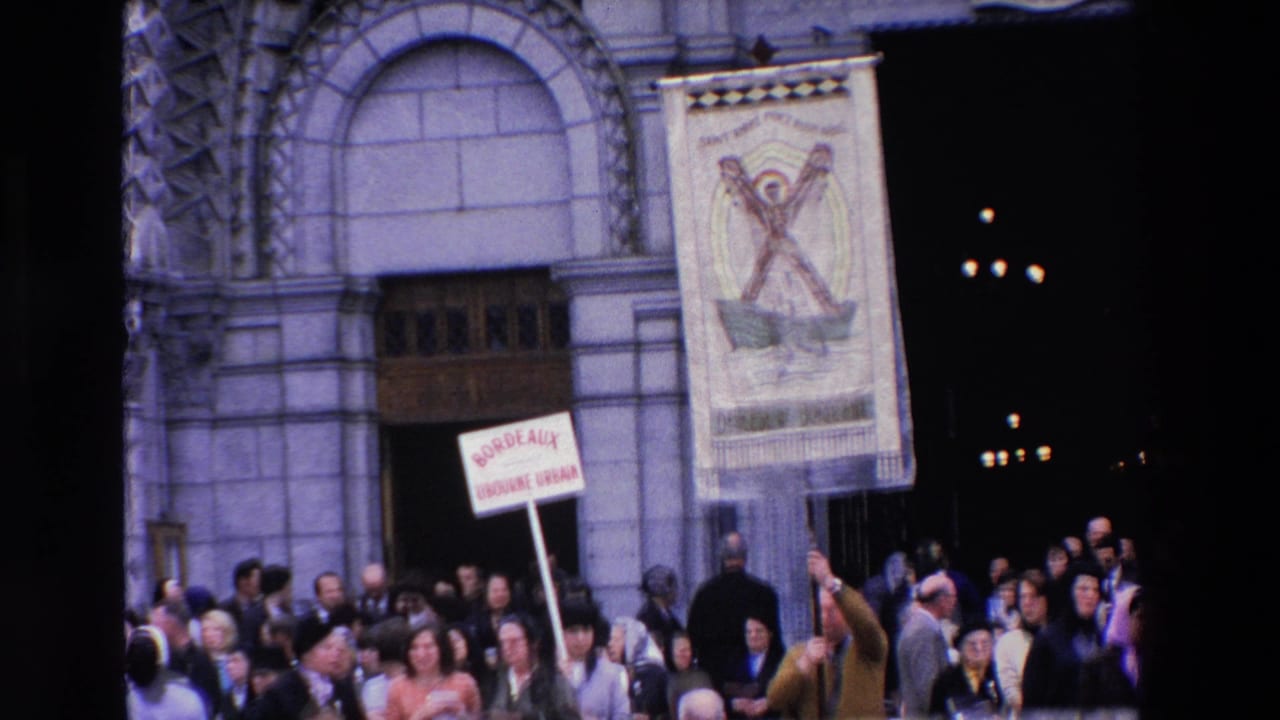 Crowd stands below a stone building facade with a raised placard.