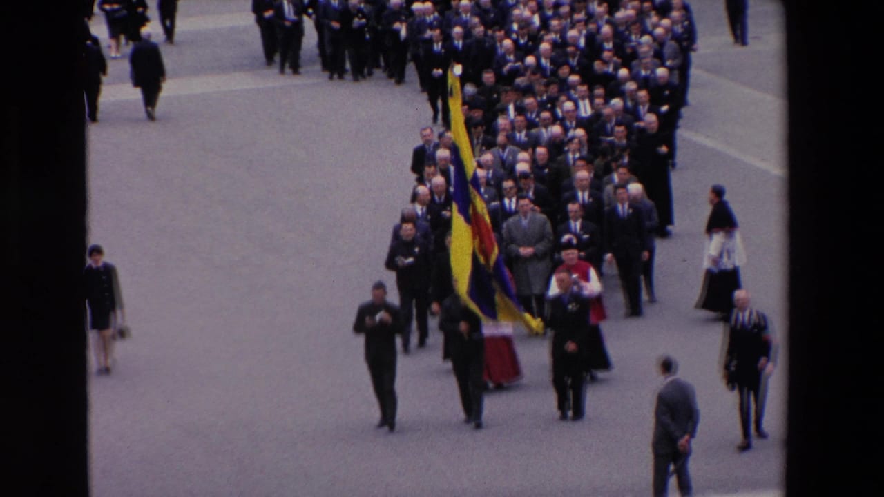 Elevated 1969 Paris home-movie view of a formal religious procession, with suited men and clergy walking behind a large yellow and blue flag.