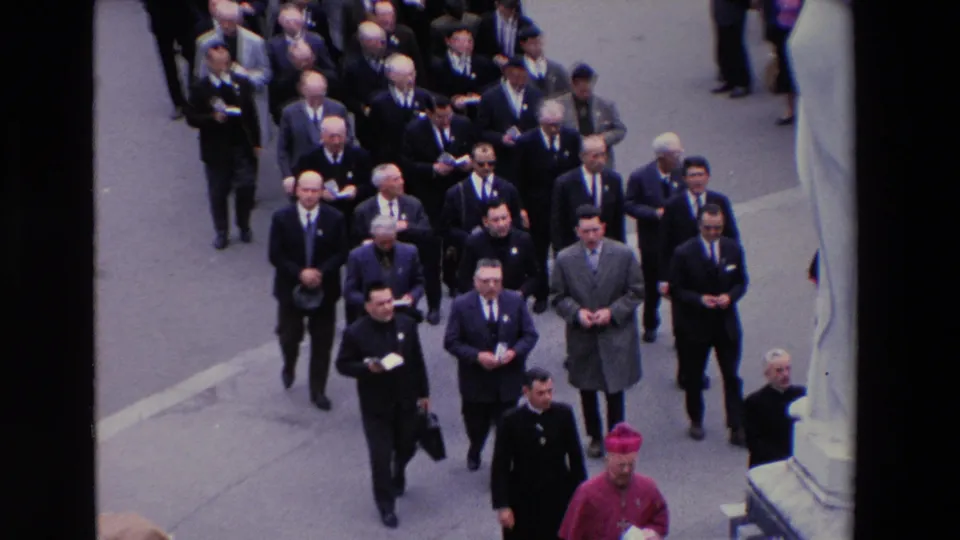 Paris 1969 home-movie frame showing an overhead view of clergy, suited participants, and the bishop at the lower edge of a formal religious procession.