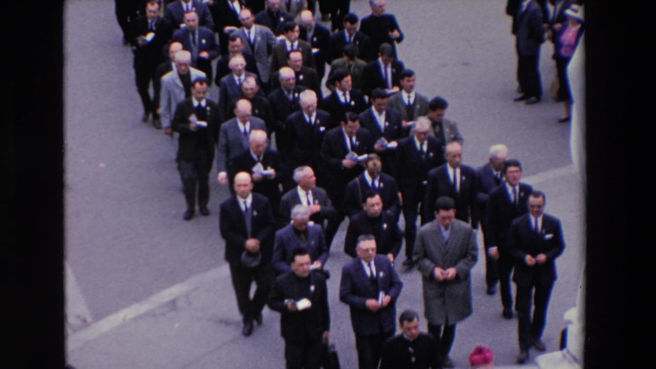 High-angle 1969 Paris 8mm frame showing rows of men in suits and ties walking in a formal street procession, with some carrying small papers.