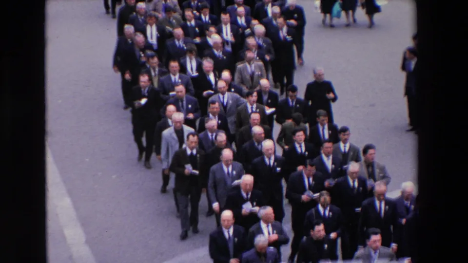 High-angle Paris street frame from 1969 showing a dense procession of suited men moving forward, with a few pedestrians visible around the edges.