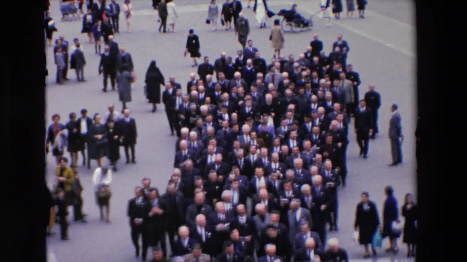1969 Paris high-angle home-movie frame showing the procession continuing down the street, with suited men packed closely together and onlookers standing nearby.