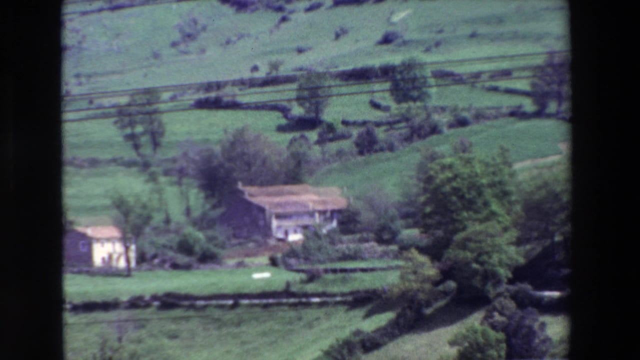 Terraced green fields with isolated rural buildings, trees, and power lines crossing the slope.