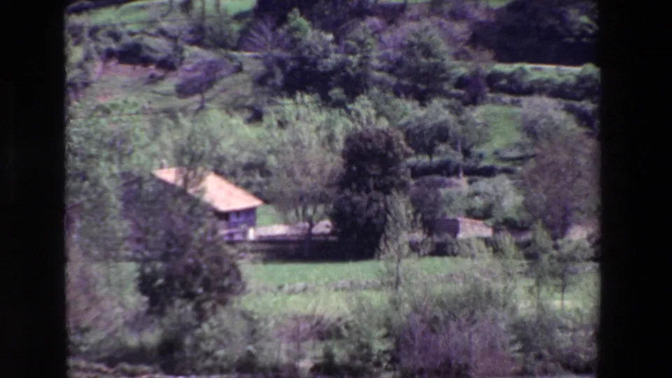 The final frame settles on a small terracotta-roofed rural house among trees, hedges, and green fields in the Spanish countryside.