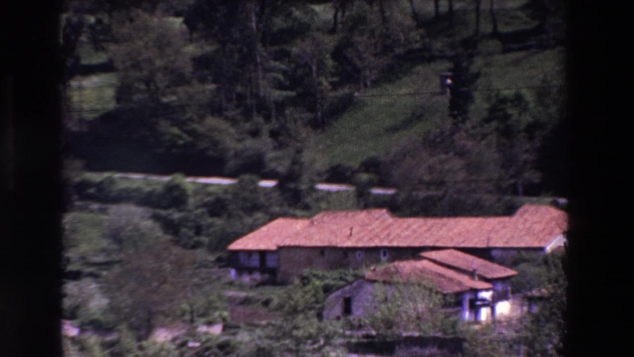 Rural red-roofed building seen from a distance in hilly greenery.