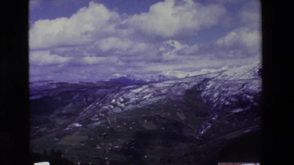 A wide 8mm view from the mountain roadside shows snow-dusted slopes, a valley, utility poles, and large clouds over the Puerto del Escudo landscape.