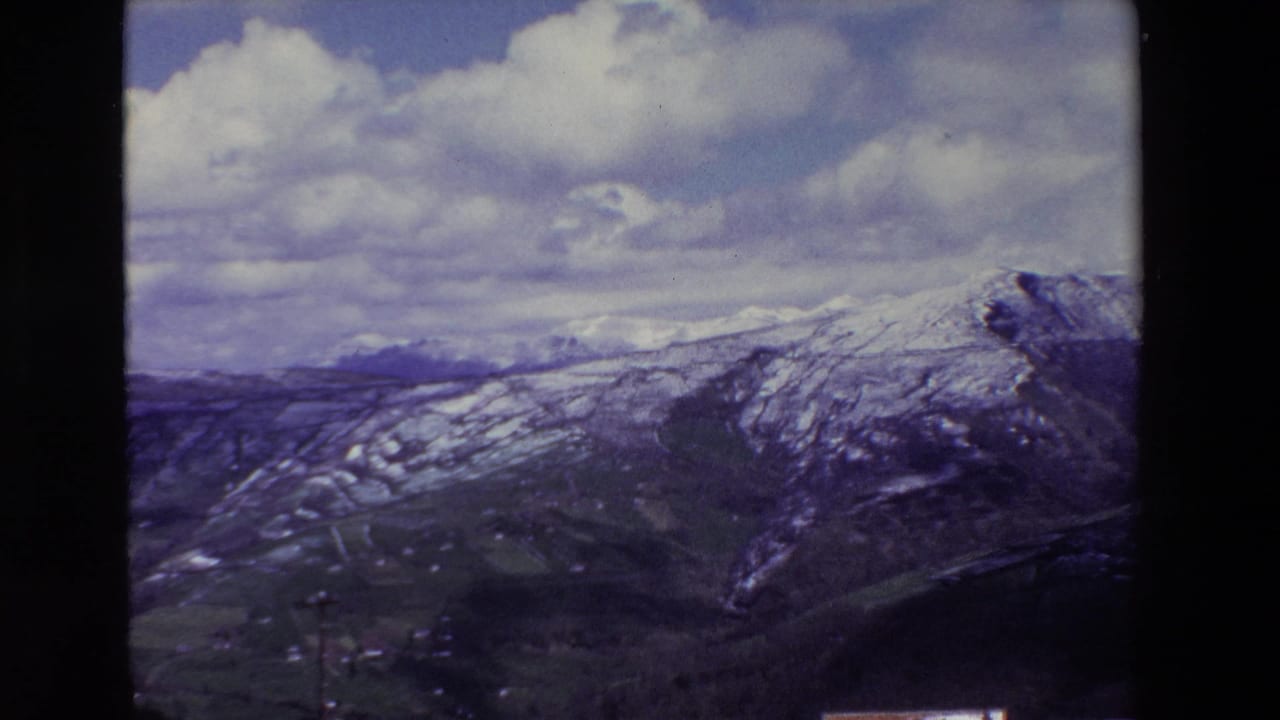 Wide mountain panorama with snow patches, valley slopes, and cloudy sky.