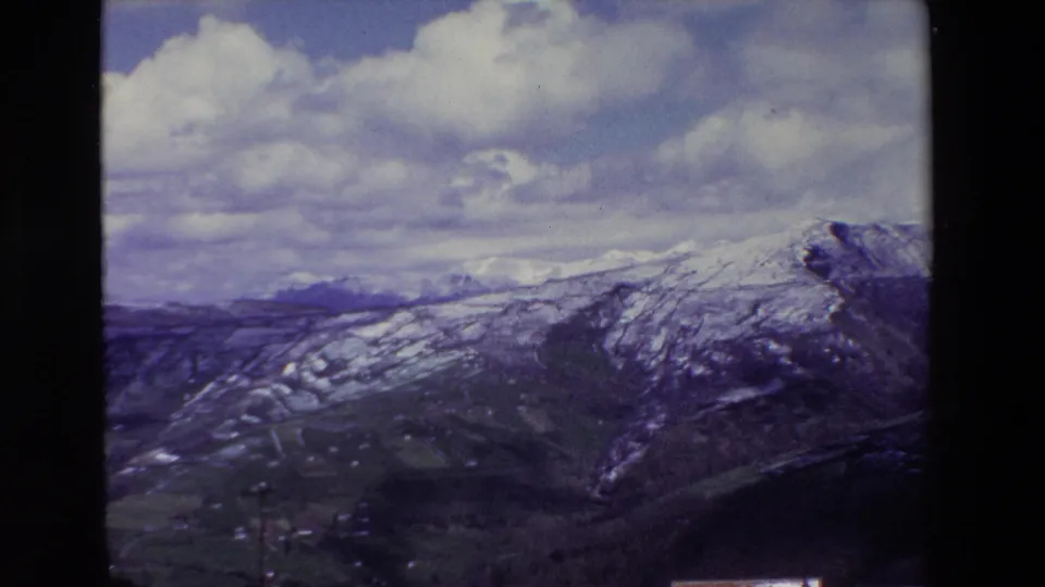 A wide 8mm scenic view appears to look across snow-patched mountains and valley terrain in Spain, with soft focus, grain, and a cloudy sky.