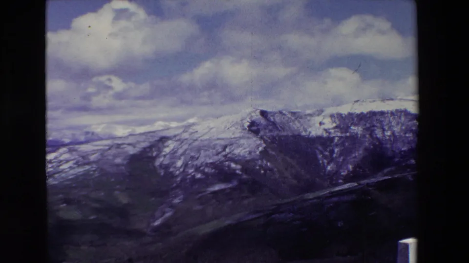 A late clip frame shows a snow-marked ridge, green valley floor, and layered clouds, with visible 8mm frame edges and slight color fading.