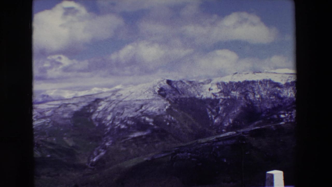 Snow-covered mountain ridge and deep gorge under clouds, with a white roadside post at the lower right.