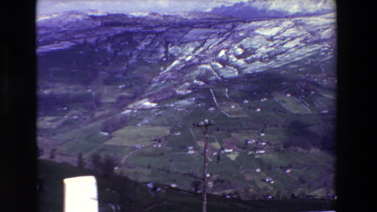 Rural valley and snow-streaked mountain slope framed by dark 8mm film edges.