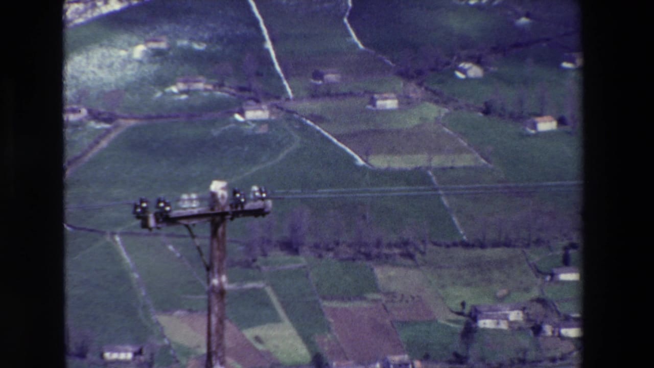 Patchwork fields and small buildings with a utility pole crossing the view.