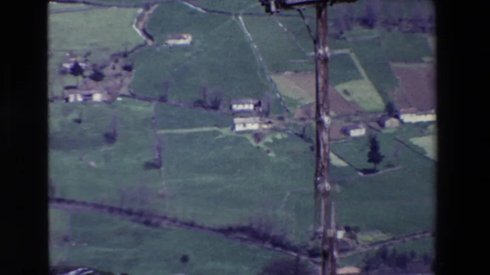 1969 8mm rural view over patchwork fields, scattered farm buildings, hedgerows, and a prominent wooden utility pole in the foreground.