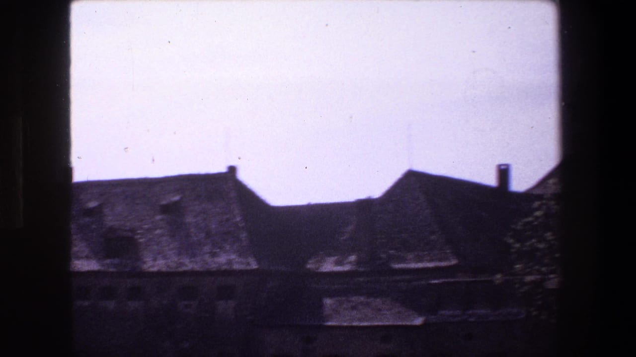 1970 Strasbourg 8mm frame showing weathered sloped-roof buildings partly obscured by dark foreground framing near a still body of water.